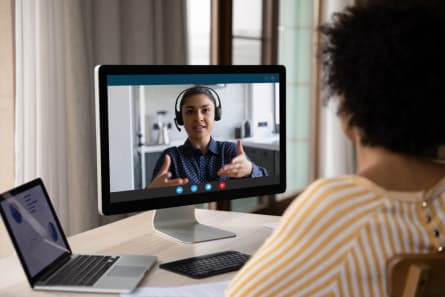 Person attending a video call on a desktop computer with a headset speaker on screen.