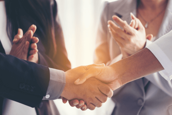 Business handshake with colleagues applauding.