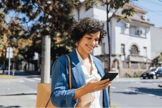 Woman smiling while looking at her phone outdoors.